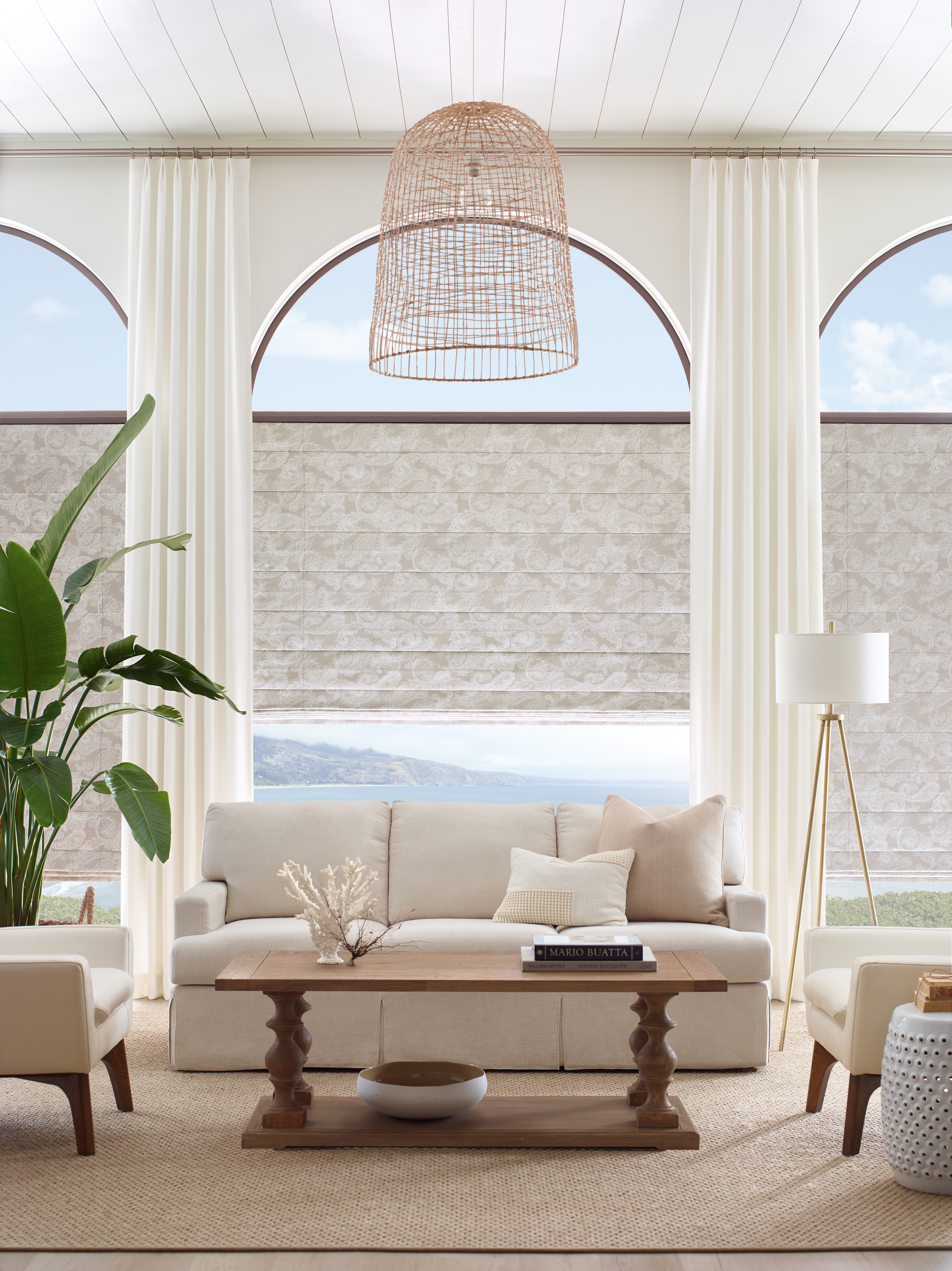 beautiful cream white beach feeling room with hunter douglas shading and interior design couch, coffee table, rug, plants, warm sunlight peaking through