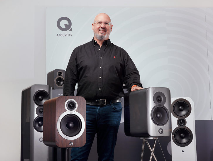 Colin Greene smiling and standing amongst Q Acoustics speakers